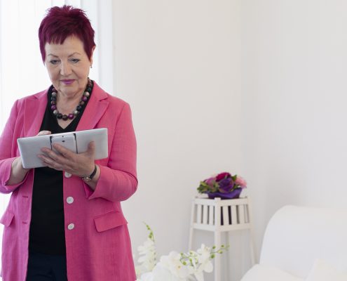 Rechtsanwältin Karin Schwarz-Feuring steht im Büro und arbeitet mit einem Tablet. Im Hintergrund sieht man Blumen.