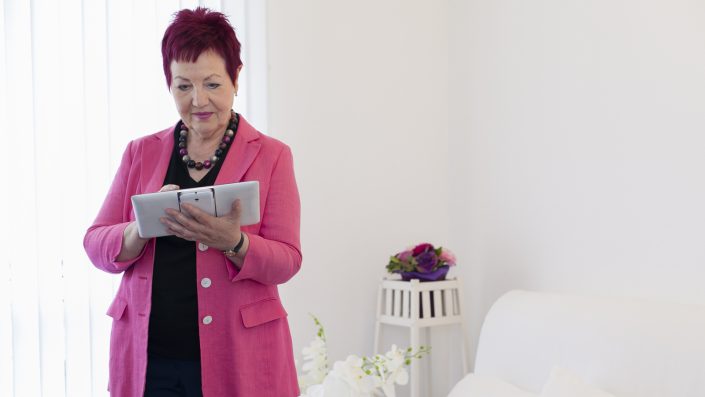 Rechtsanwältin Karin Schwarz-Feuring steht im Büro und arbeitet mit einem Tablet. Im Hintergrund sieht man Blumen.