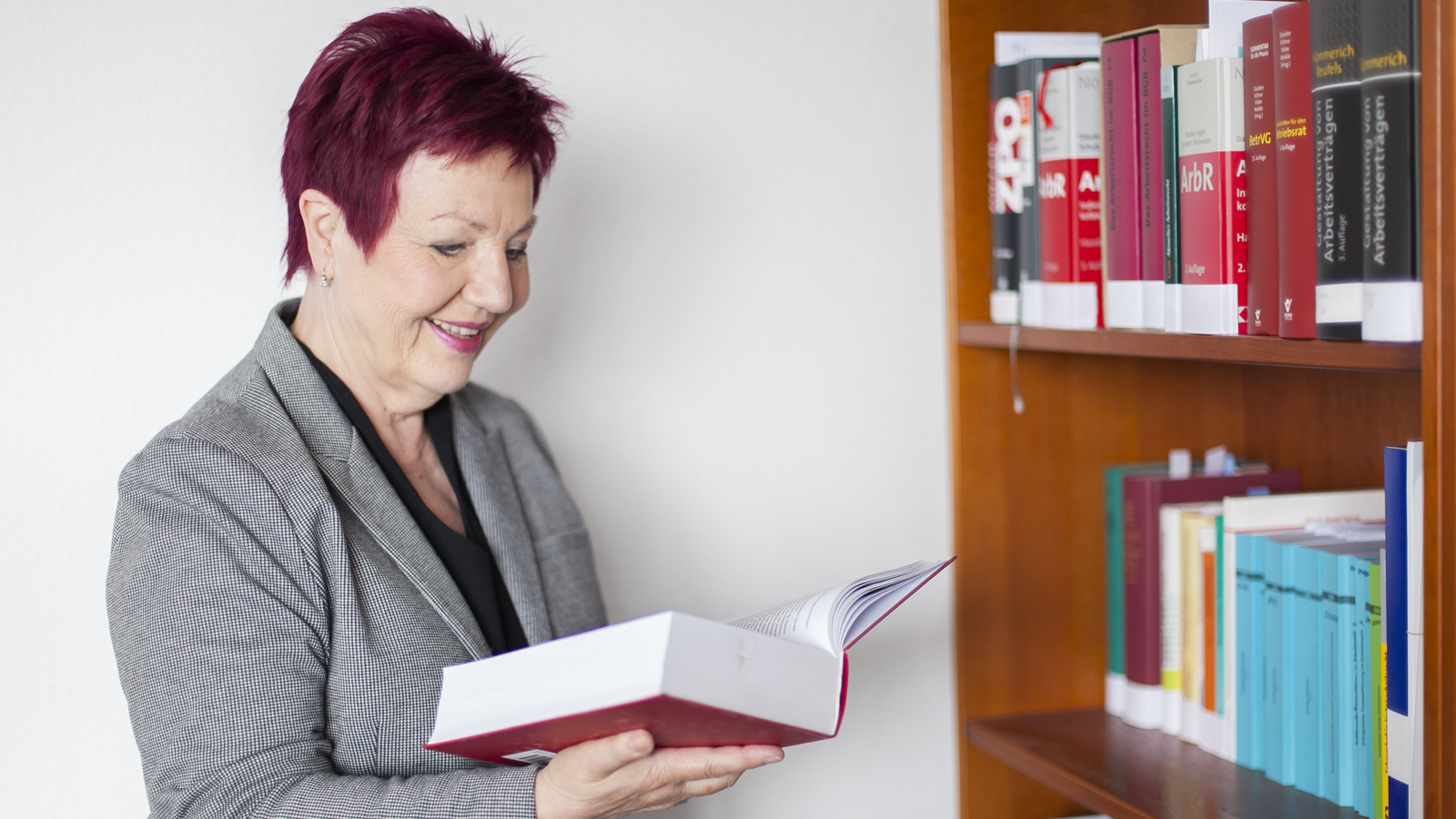 Die Anwältin hält ein Buch in der Hand, liest und steht vor eine Bücherregal.