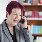 Frau Schwarz-Feuring telefoniert. Im Hintergrund steht ein Bücherregal.