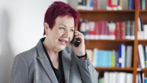 Frau Schwarz-Feuring telefoniert. Im Hintergrund steht ein Bücherregal.