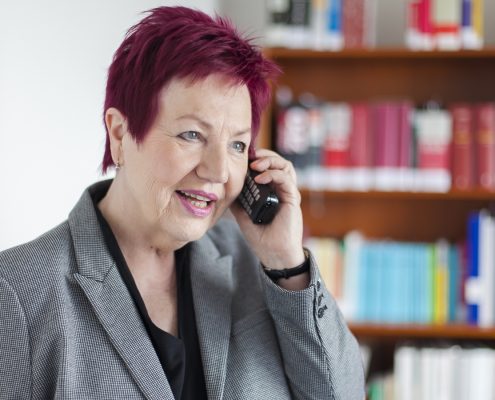 Frau Schwarz-Feuring telefoniert. Im Hintergrund steht ein Bücherregal.