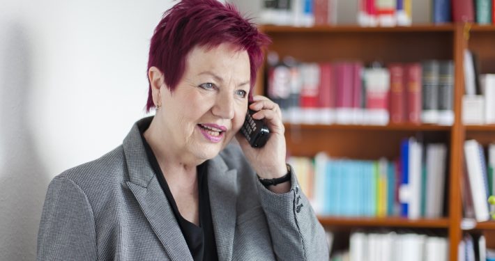 Frau Schwarz-Feuring telefoniert. Im Hintergrund steht ein Bücherregal.