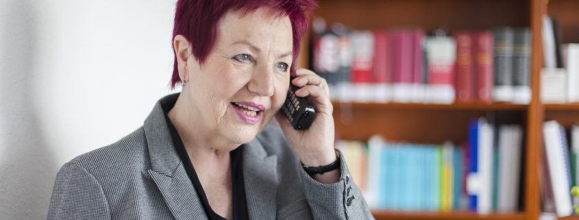 Frau Schwarz-Feuring telefoniert. Im Hintergrund steht ein Bücherregal.